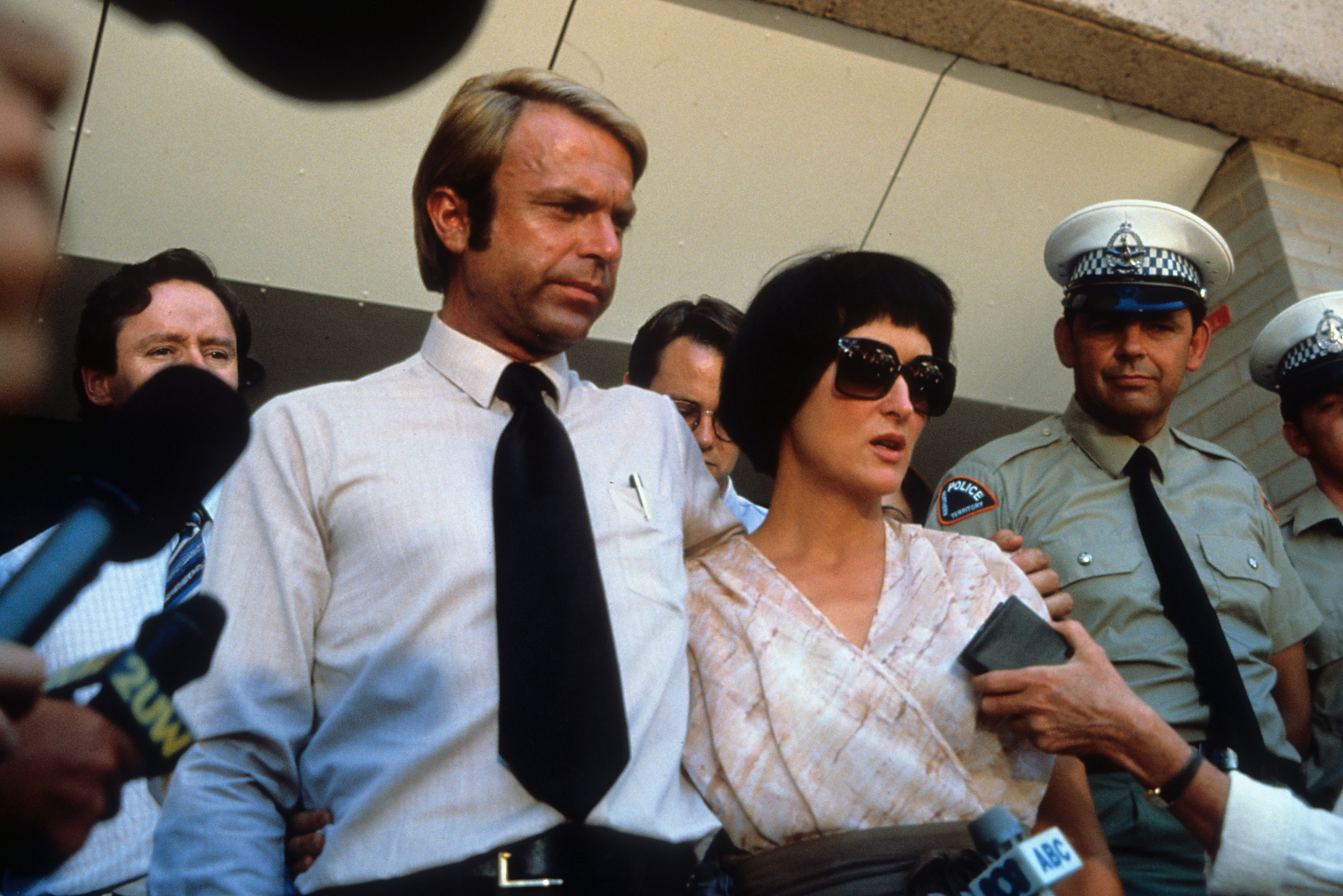 Man and a woman (in a film) interviewed by press outside a police station