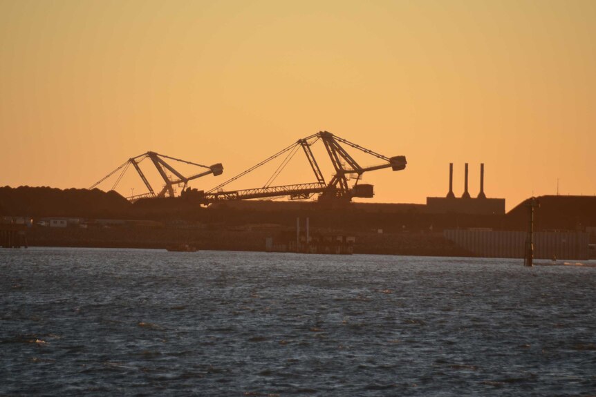 Two bucket-wheel excavators are pictured at sunset on the far side of a harbour.