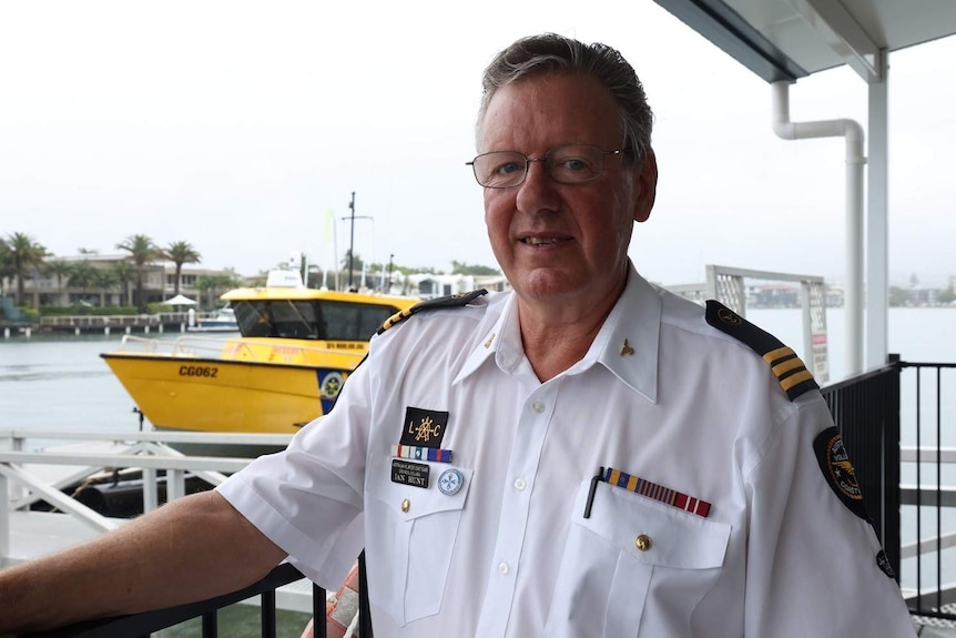 A man wearing a coast guard shirt stands in front of a yellow patrol boat.