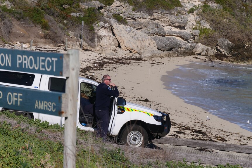 A man in uniform stands next to a ute parked on a beach