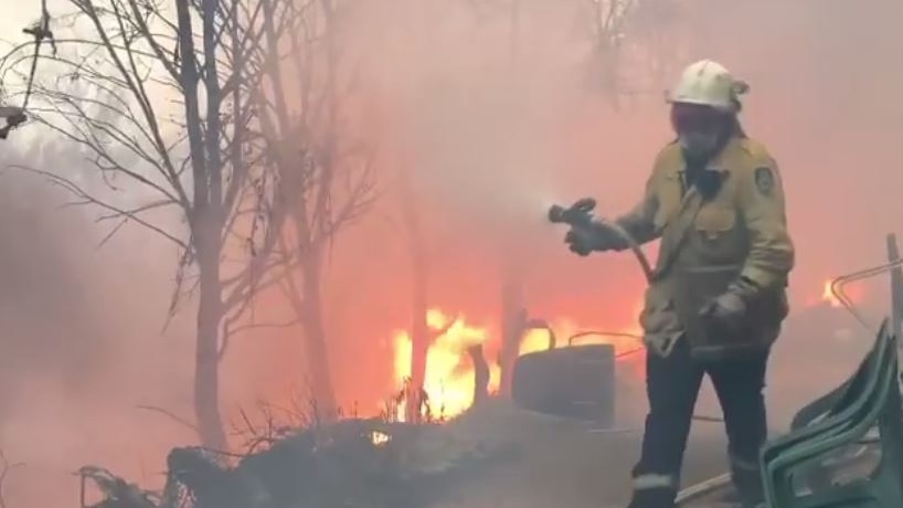 A firefighter carries a hose as flames surround a house