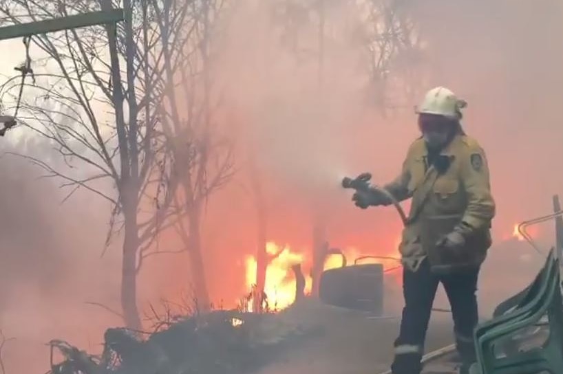 A firefighter carries a hose as flames surround a house