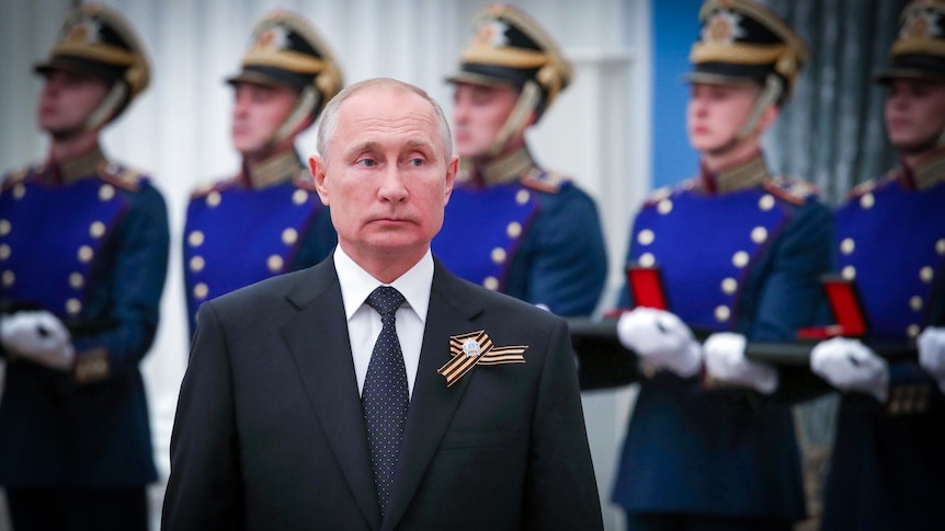 Vladimir Putin standing in front of a row of Russian troops in dress uniforms