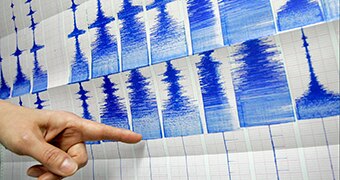 A hand pointing to a seismograph, with earthquake tremors graphed in blue ink on paper.