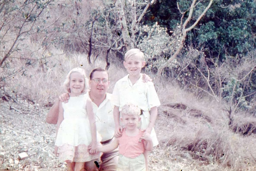 A vintage photograph shows a father kneeling down with his children, and all of them are smiling at the camera.