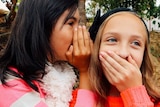 A girl whispers into her shocked friends ear