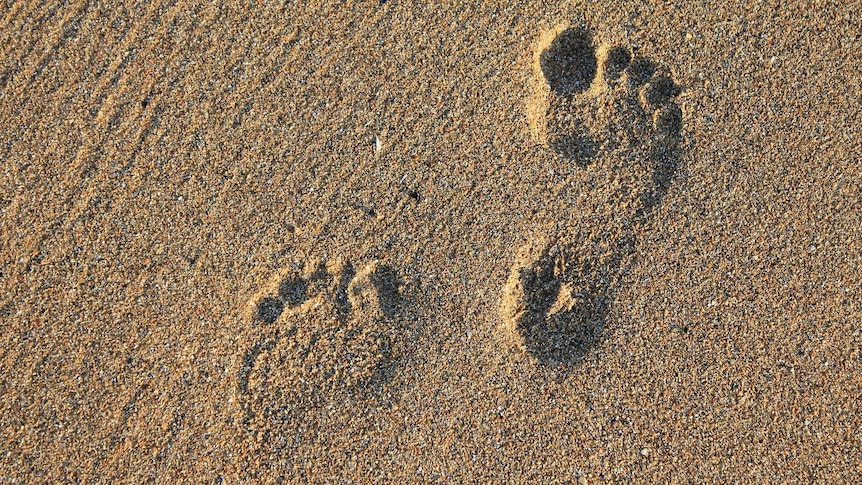 Two bare footprints in course sand, one is much more pronounced than the other