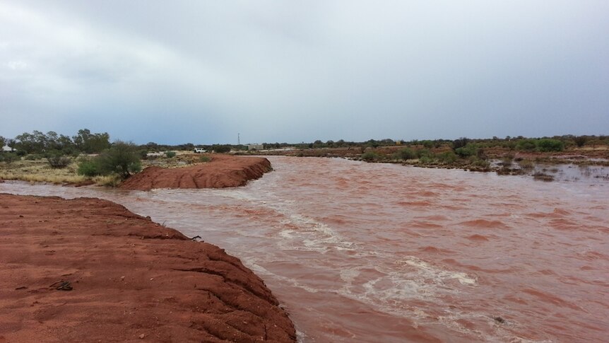 muddy floodwaters running through red dirt of central australia