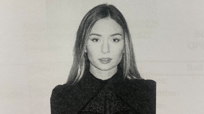A young, blonde woman wearing a dark top in a grainy, black and white mugshot.