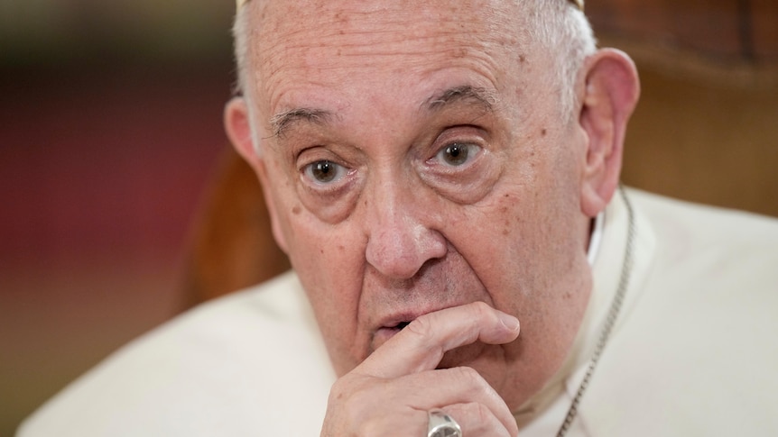 A close-up of Pope Francis with his finger on his chin.