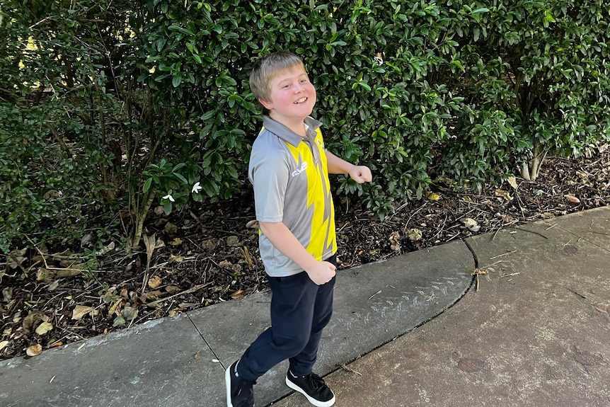 Boy dancing and smiling on pathway in botanic gardens. 