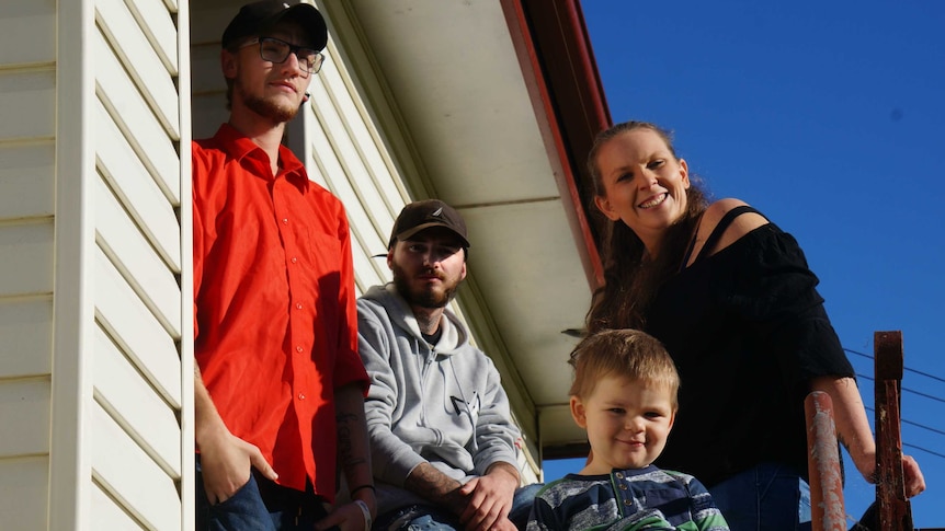 Four people stand in the sun on a front porch.