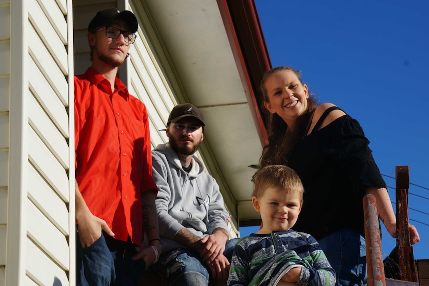 Four people stand in the sun on a front porch.