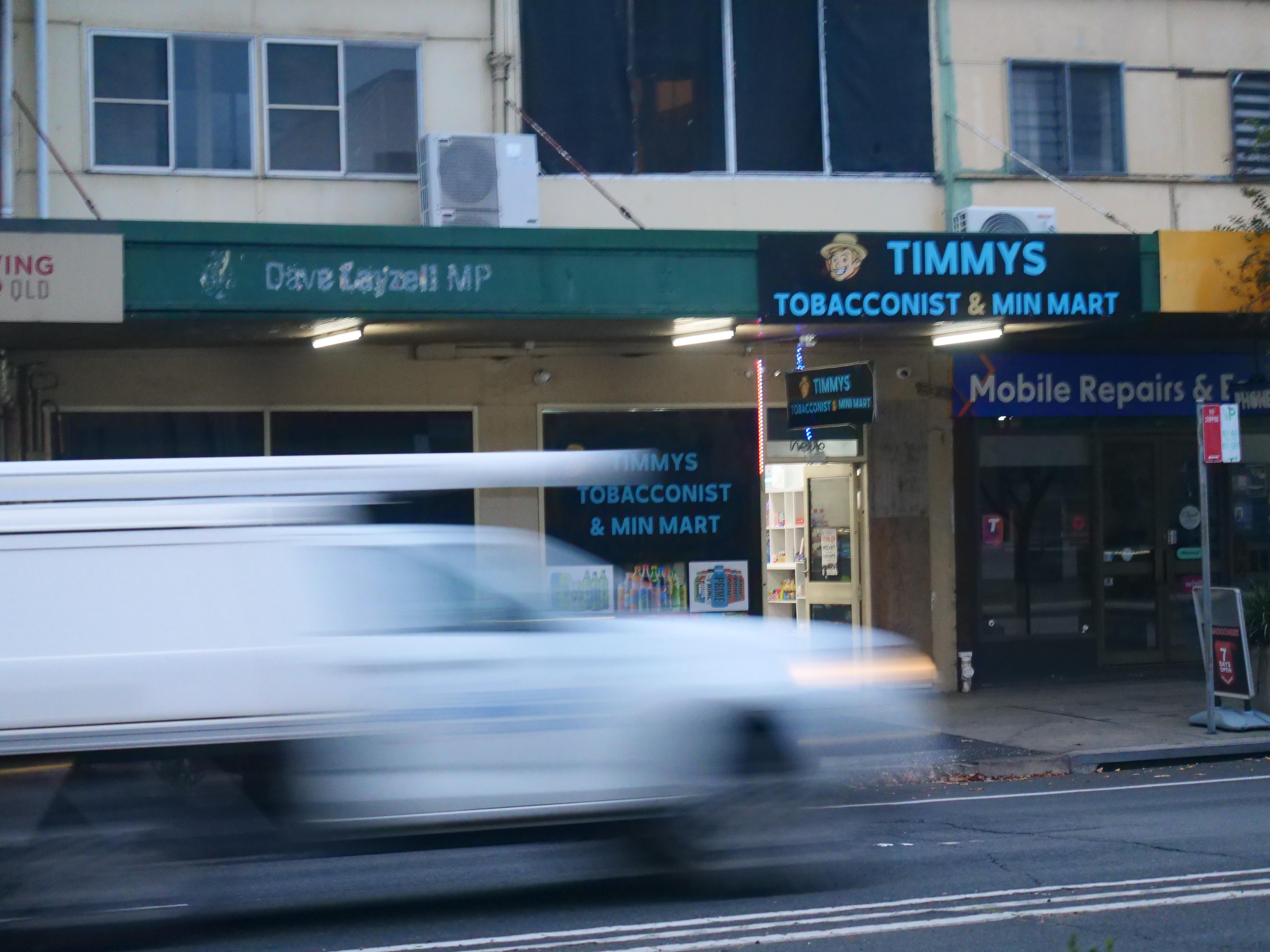 A blurred van passes a row of shops.