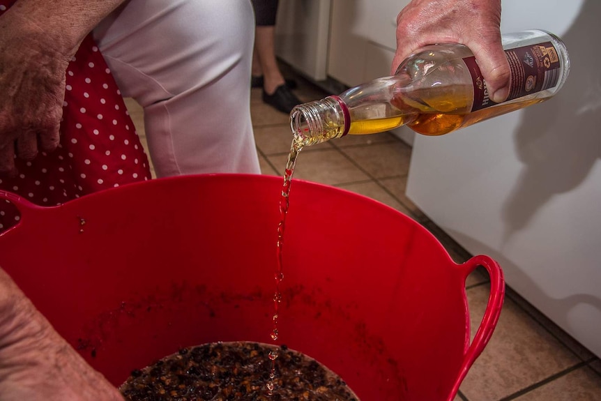 A hand pouring brandy into a big tub with pudding mix