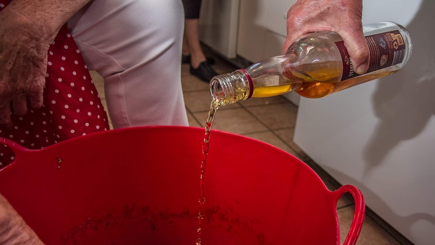 A hand pouring brandy into a big tub with pudding mix