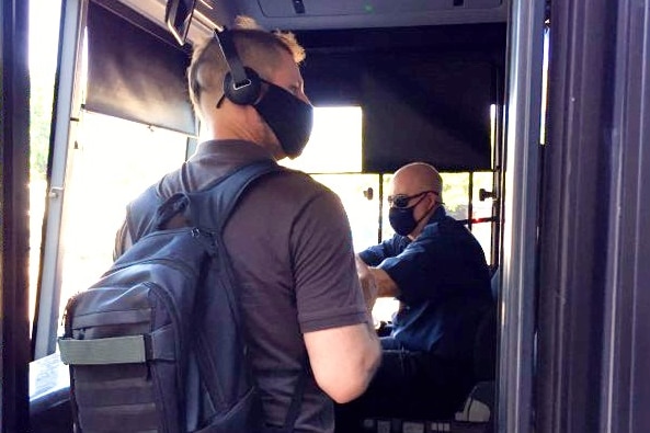 A man in a mask gets on a bus where the driver is also wearing a mask