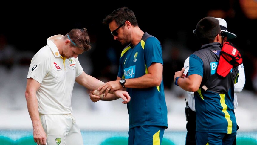Steve Smith is checked out by the team physio after copping a short ball to his unguarded forearm