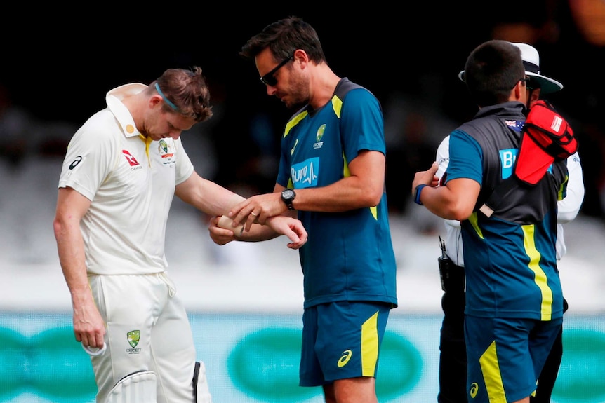 Steve Smith is checked out by the team physio after copping a short ball to his unguarded forearm