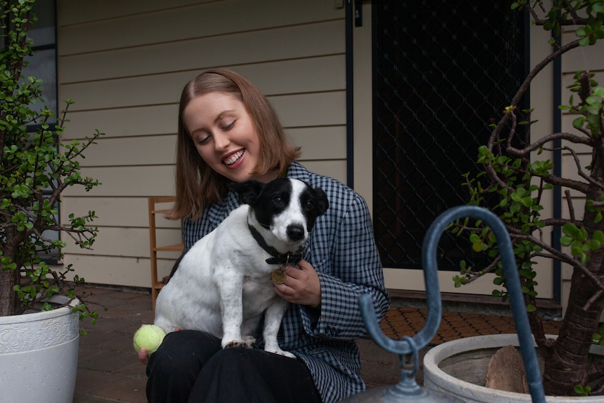 A young person smiles at a dog on their lap.