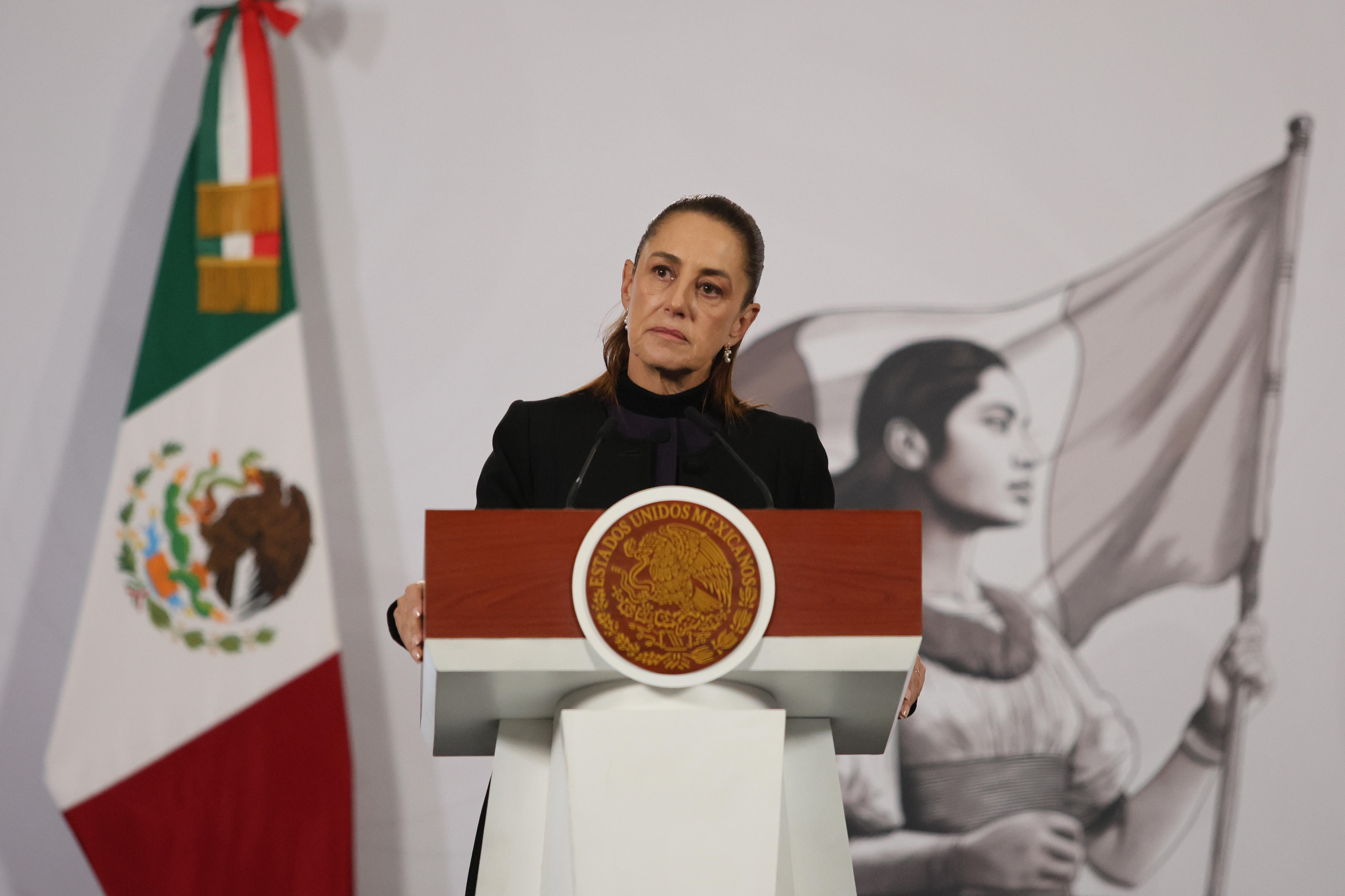 Claudia Sheinbaum standing at a podium with the Mexican flag behind her.