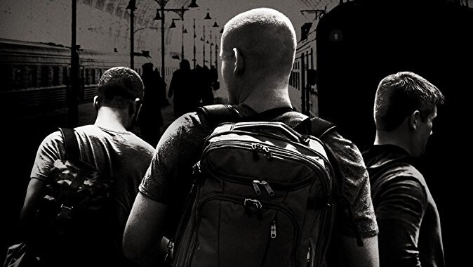 A movie poster shows three men from behind on a train platform