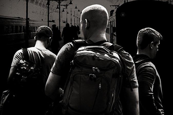 A movie poster shows three men from behind on a train platform