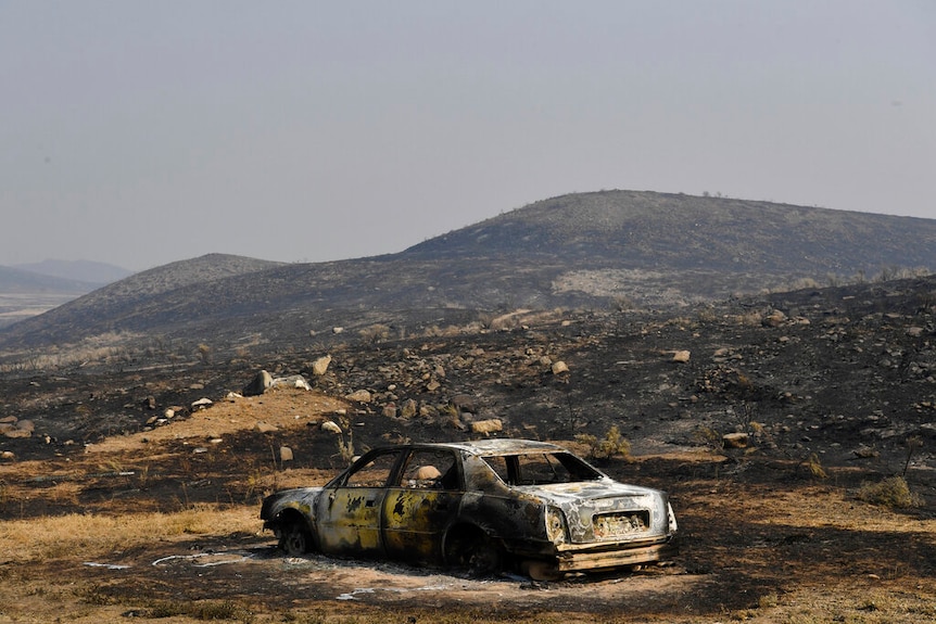 You see a charred sedan sitting on a barren blackened mountaintop with the sky clogged in fire smoke.