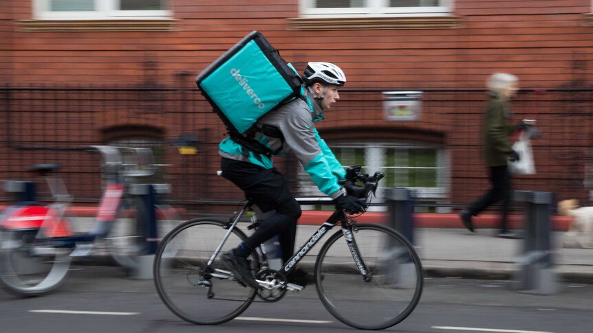 A man wearing a Deliveroo backpack rides down a London street.