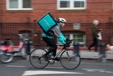 A man wearing a Deliveroo backpack rides down a London street.