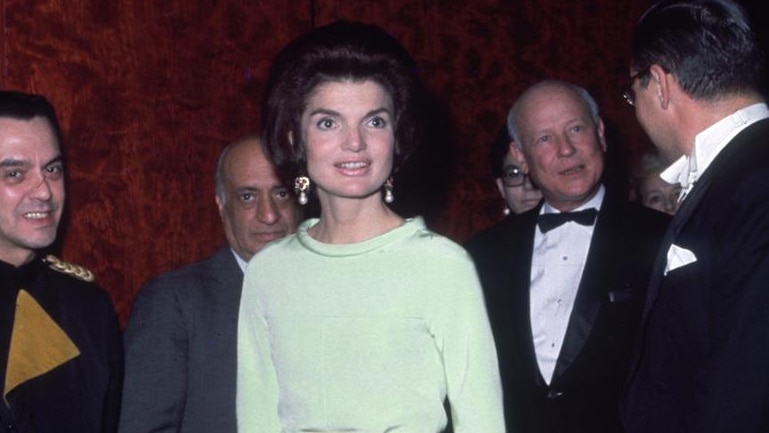 Jacqueline Kennedy stands in front of a group of men in a green Givenchy dress.