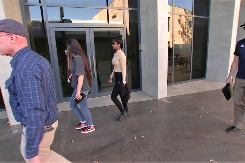 two men wearing caps and two women walk toward the glass doors of the Alice Springs Supreme Court