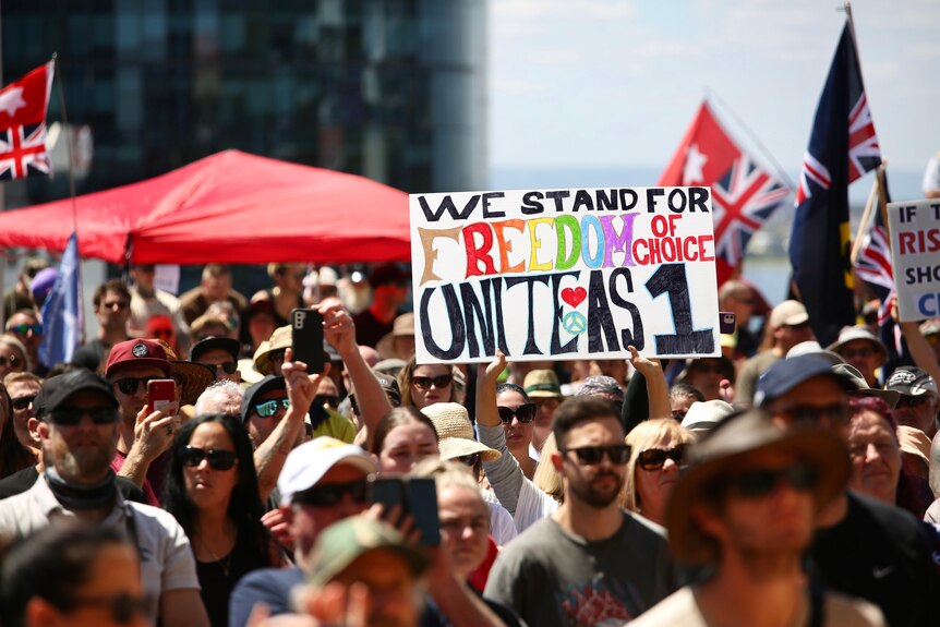 A crowd of protesters outdoors in Perth with one holding a sign reading 'We stand for freedom of choice, Unite as 1'.