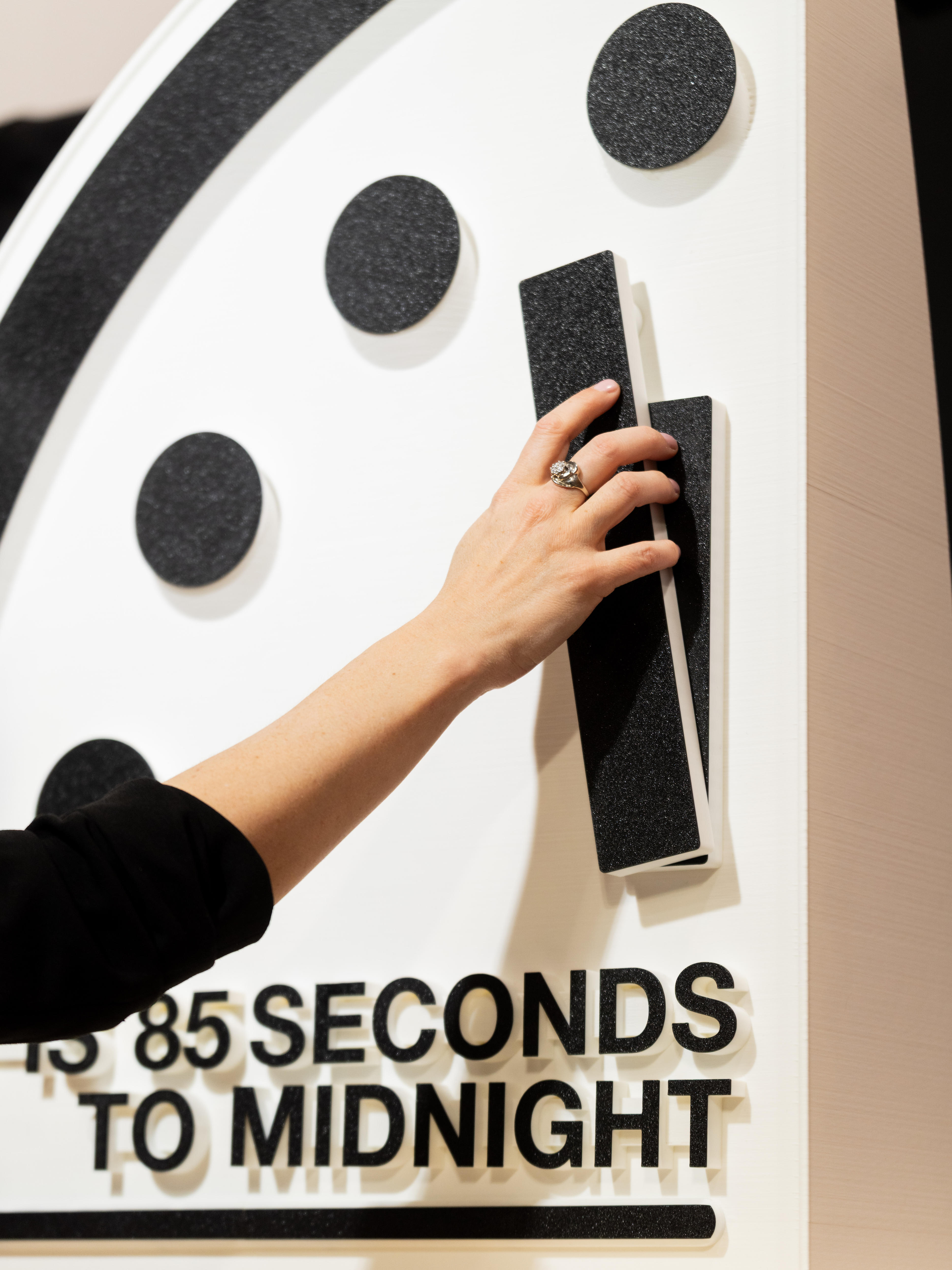 A human hand moves the minute hand on a model clock towards midnight.