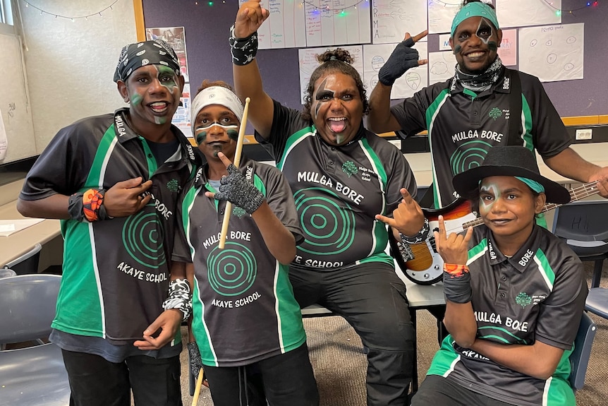 Six Indigenous musicians wearing matching green and black polo shirts and wearing green and black facepaint.