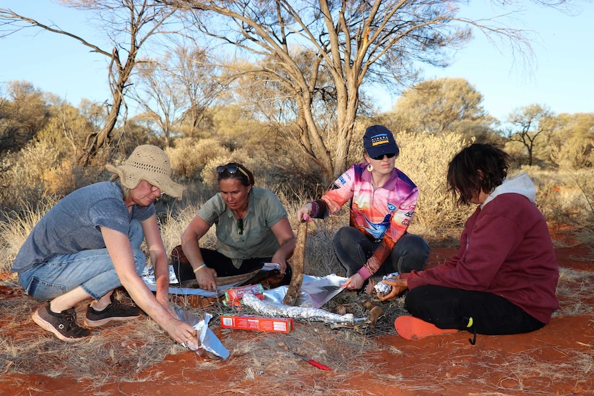 Four women cooking kangaroo tail on a fire.