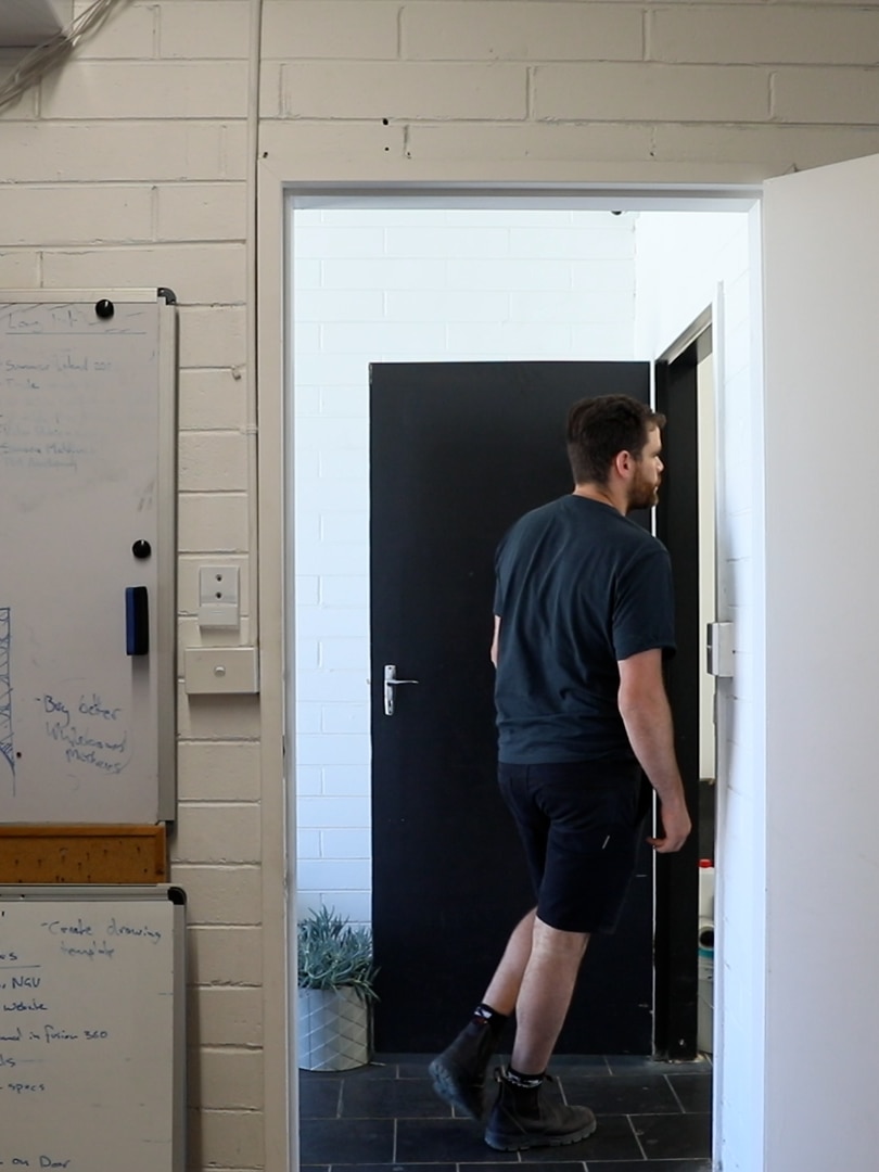 In a dim office, you view a whiteboard adjacent to a door frame with a man walking through it.