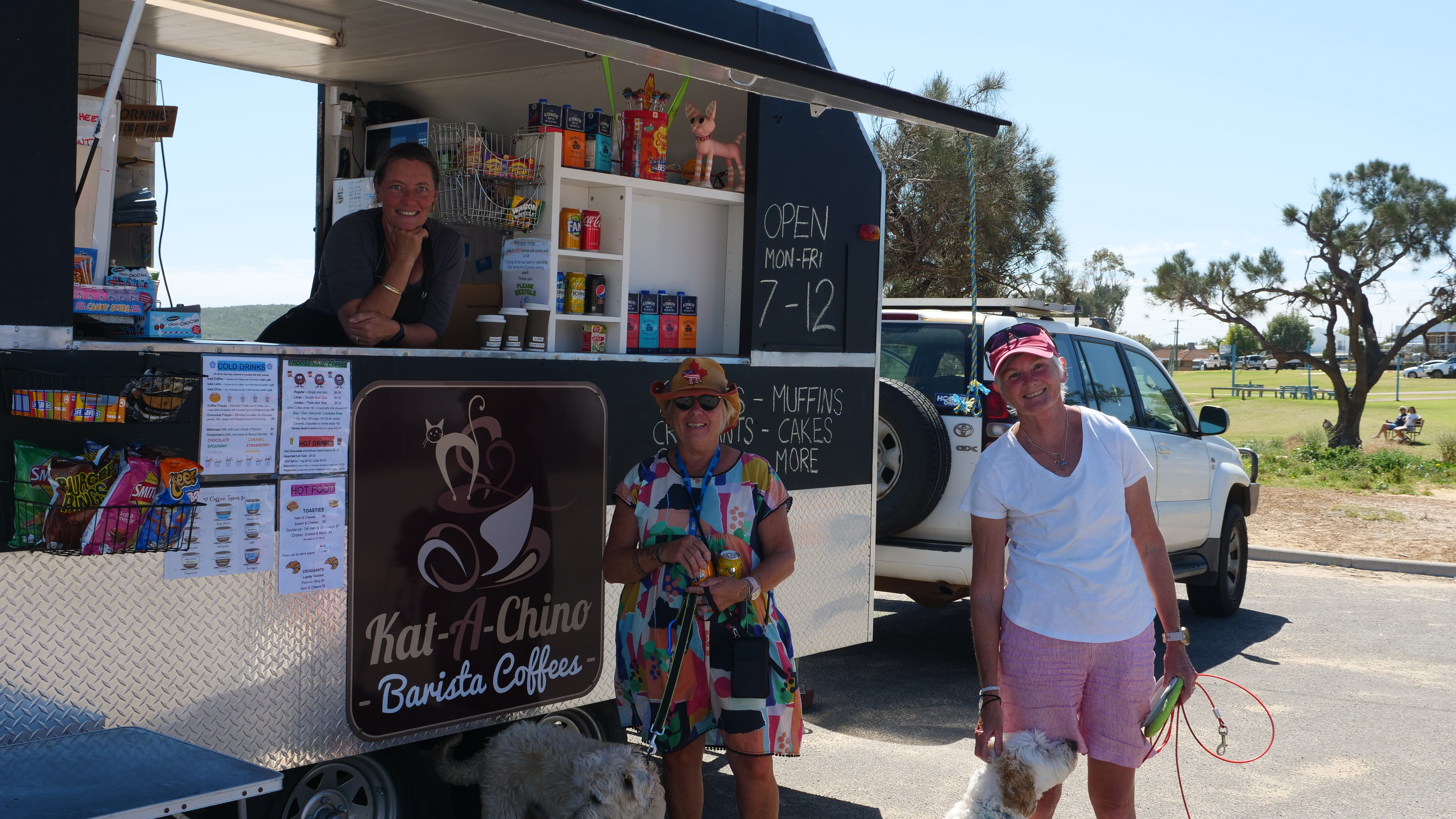 Tourists at a coffee van that has a woman who is at the counter, smiling.