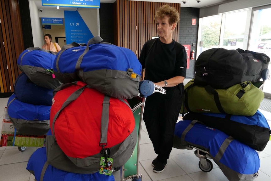 A woman stands amid three large luggage trolleys in an airport building. each trolley is stacked high with bags