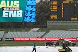 A player jogs across the field as groundsmen cover a cricket pitch amid rainfall