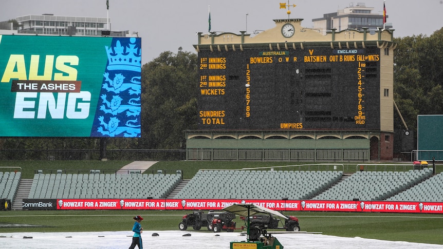 A player jogs across the field as groundsmen cover a cricket pitch amid rainfall