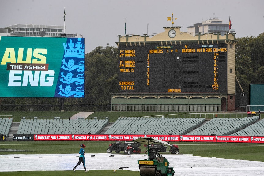A player jogs across the field as groundsmen cover a cricket pitch amid rainfall