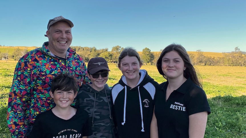 A man and four primary to high school aged children standing in a paddock smiling.