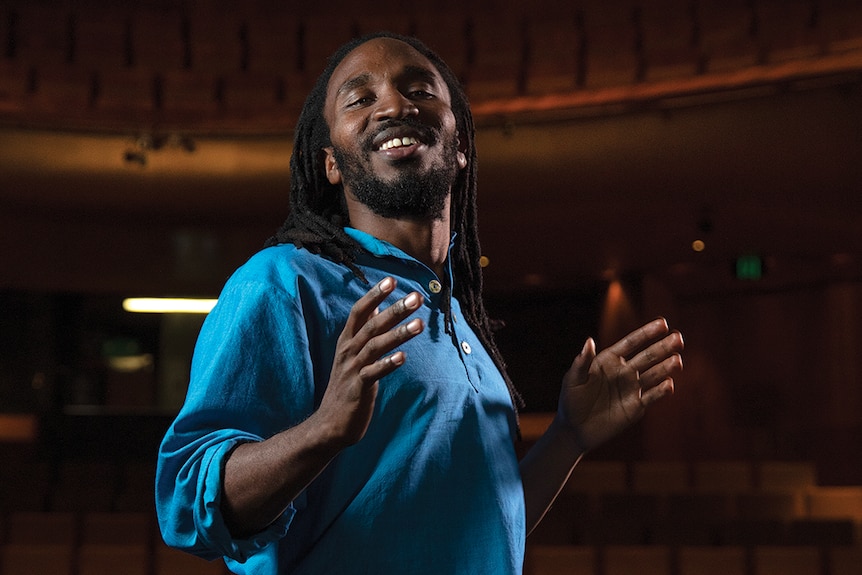 Writer and performer Mararo Wangai on a stage in an empty auditorium, arms out in performance