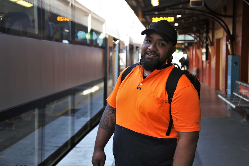 A man in an orange shirt waiting to board a train in Sydney