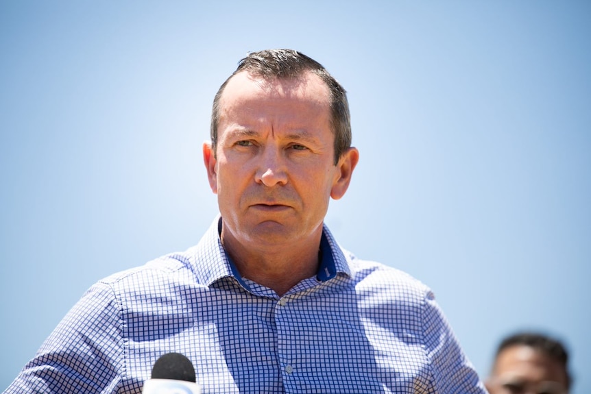 Mid shot of Mark McGowan looking to the distance, wearing a blue and white checked shirt. 