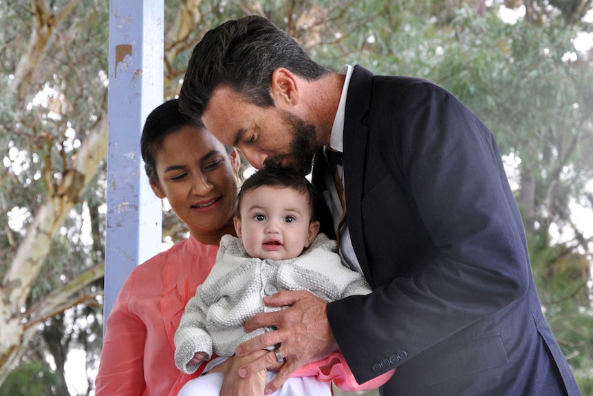 Tim Hammond kisses his baby son's head while standing alongside his wife.