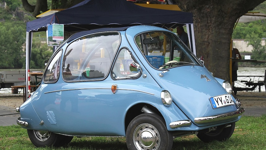 Image of a blue 1957 Heinkel Kabine bubble car sitting on grass in front of a river.