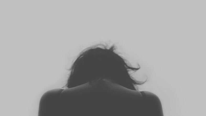 Black and white image of woman with her head bent, shot from behind.