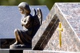 A small statuette of a weeping angel sits atop an unidentified gravestone in a cemetery.
